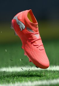 Leuchtend orangefarbener Fußballschuh mit strukturierter Oberfläche, silbernen Akzenten und einem Logo, Schnürsenkeln sowie einem schlanken, aerodynamischen Design.