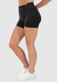 Zwart hoogtaille shorts van rekbaar materiaal, met een gladde textuur en naadloos ontwerp. Gecombineerd met witte sportschoenen.