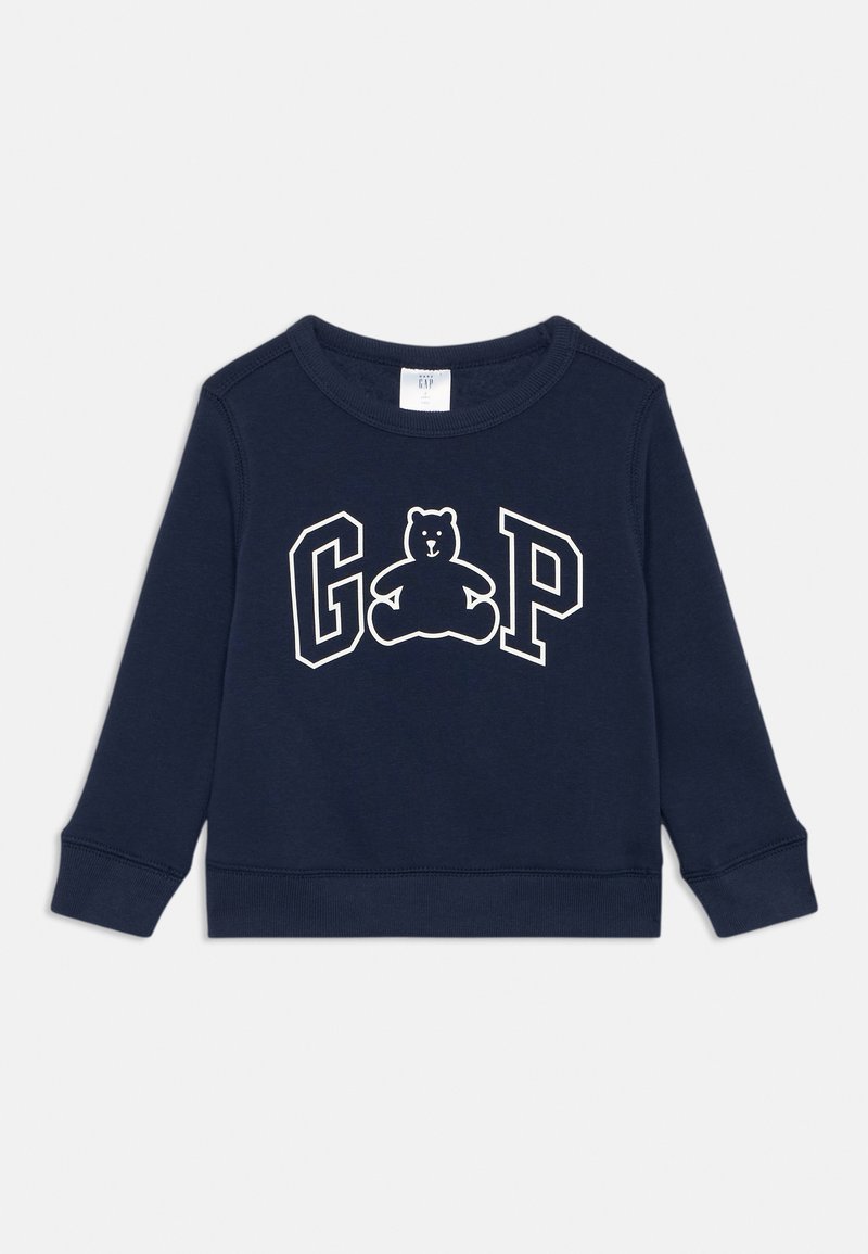 Sweat-shirt bleu marine avec un col rond, des manches longues, des poignets côtelés, et un graphique à l'avant représentant un ours avec l'inscription "GAP" en blanc.