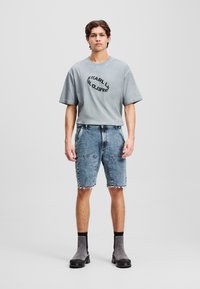 T-shirt gris à manches courtes avec un graphique noir circulaire. Short en denim avec des bords effilochés et deux poches avant. Bottines grises à la cheville.