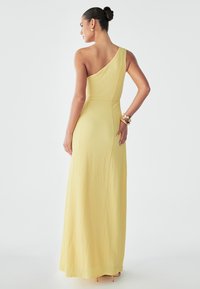 Yellow maxi dress with a textured surface, featuring a single shoulder strap and a fitted bodice, extending to a flowy hem.
