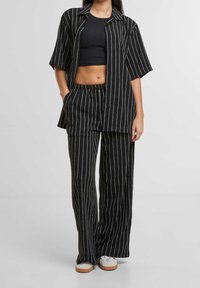 Černobíle pruhovaný dvoudílný outfit; košile s krátkým rukávem na knoflíky a kalhoty s elastickým pasem; volný střih, lehká látka.