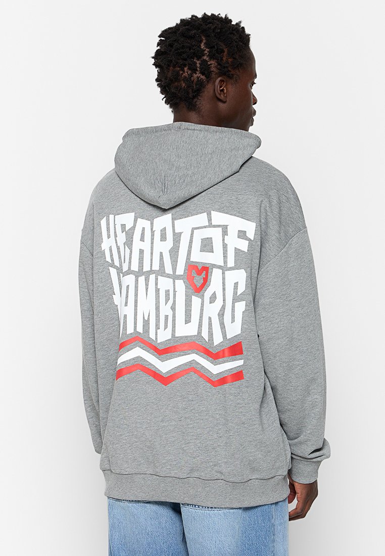 Sudadera con capucha gris que presenta un gran texto blanco y rojo "HEART OF HAMBURG" en la parte posterior, con acentos a rayas en rojo y blanco.