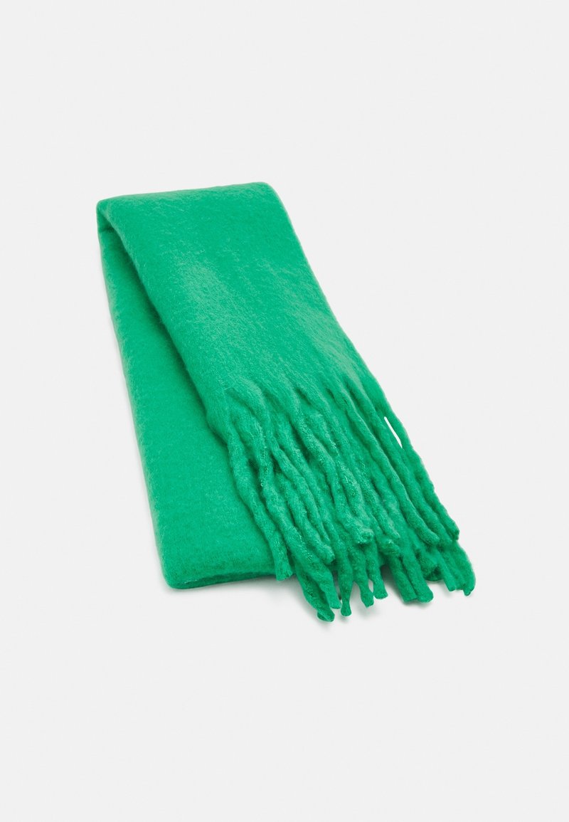 Écharpe douce vert vif avec de longues franges, pliée soigneusement sur une surface blanche.