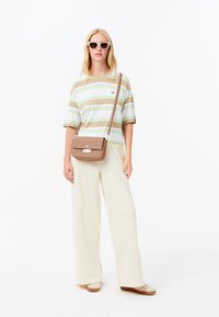 Camicia a maniche corte a righe nei colori beige, bianco e verde. Pantaloni larghi color crema. Borsa a tracolla marrone con chiusura. Occhiali da sole.