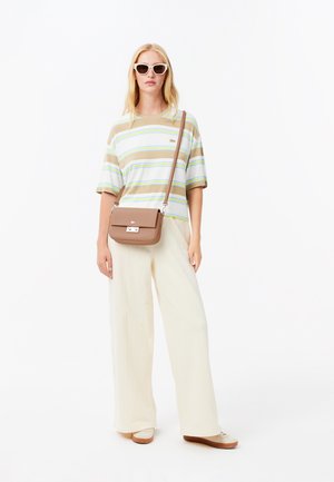 Chemise à manches courtes rayée en beige, blanc et vert. Pantalon large crème. Sac bandoulière marron avec une fermeture. Lunettes de soleil.