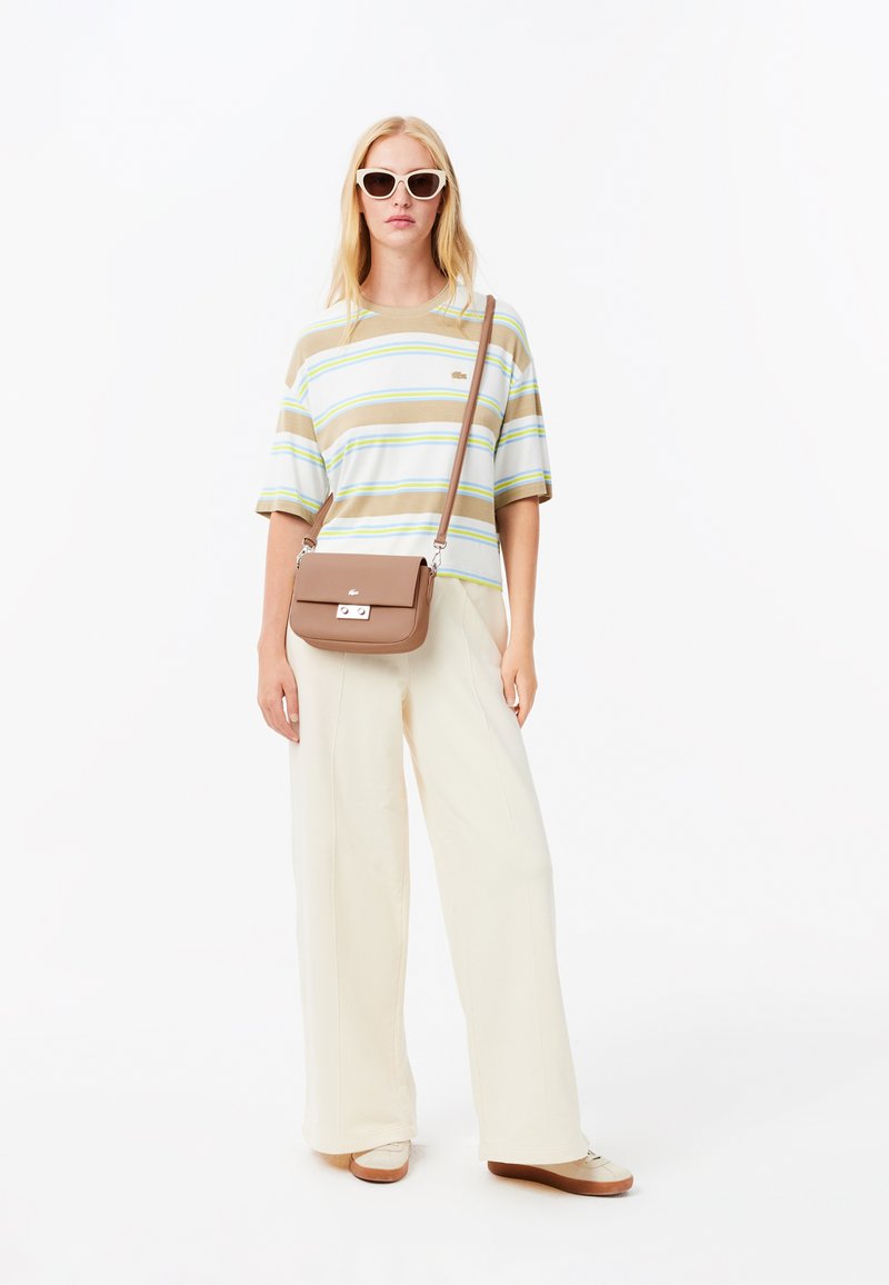 Camicia a maniche corte a righe nei colori beige, bianco e verde. Pantaloni larghi color crema. Borsa a tracolla marrone con chiusura. Occhiali da sole.