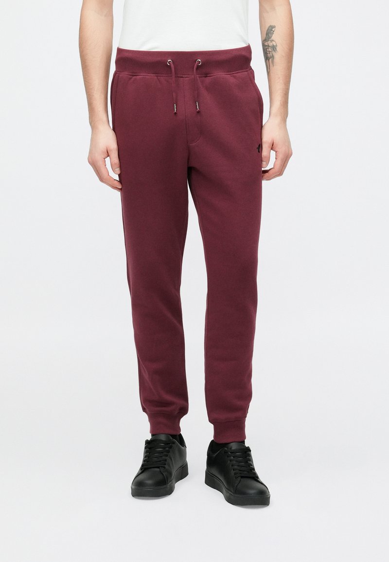 Μπεζ φόρμες μπορντό με ελαστική μέση και κορδόνι, με πλαϊνές τσέπες και μανσέτες ριμπ, κατασκευασμένες από απαλό, υφασμένο ύφασμα.