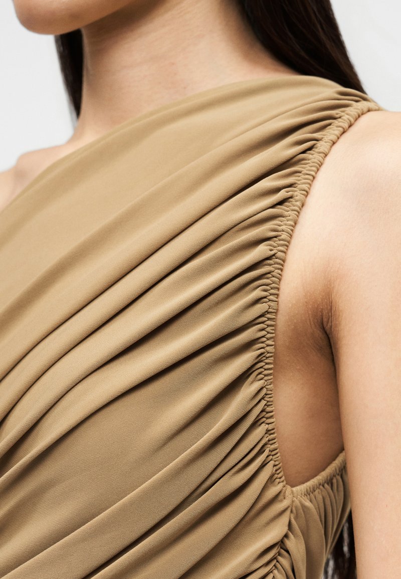 Robe asymétrique en tissu beige doux avec texture froncée, design drapé et détails élastiqués au niveau de l'encolure et de l'emmanchure.