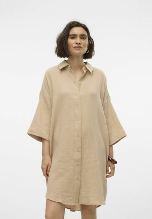 Beige oversized skjortklänning i texturerad tyg med knappslå fram, krage och vida ärmar. Har en något bågformad nederkant.