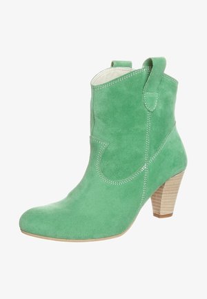Bottine en daim vert avec un bout pointu, des coutures décoratives et un talon empilé. Comprend des languettes pour un enfilage facile.