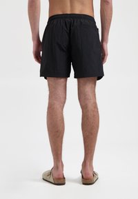 Schwarze Schwimmshorts aus leichtem Stoff, mit elastischem Bund und einer Gesäßtasche. Das Material hat eine strukturierte Oberfläche.