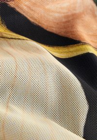 Tkanina o teksturze z siateczkowym wzorem w ciepłych odcieniach beżu, pomarańczu i czerni, podkreślona subtelnymi wzorami i różnorodnymi tonacjami.