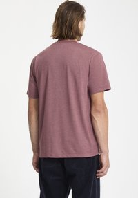 Camiseta de manga corta en color burdeos, hecha de tela suave, con un escote redondo y un corte relajado, combinada con pantalones oscuros.