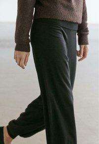 Dunkelgraue, aus weichem Stoff gefertigte Hosen mit schmal zulaufendem Design und elastischem Bund, kombiniert mit einem strukturierten braunen Pullover.