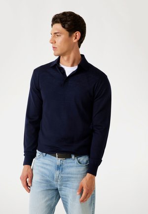 Dunkelblaues Langarm-Polohemd mit Kragen, aus strukturiertem Stoff, kombiniert mit hellblauen Jeans und einem schwarzen Gürtel.