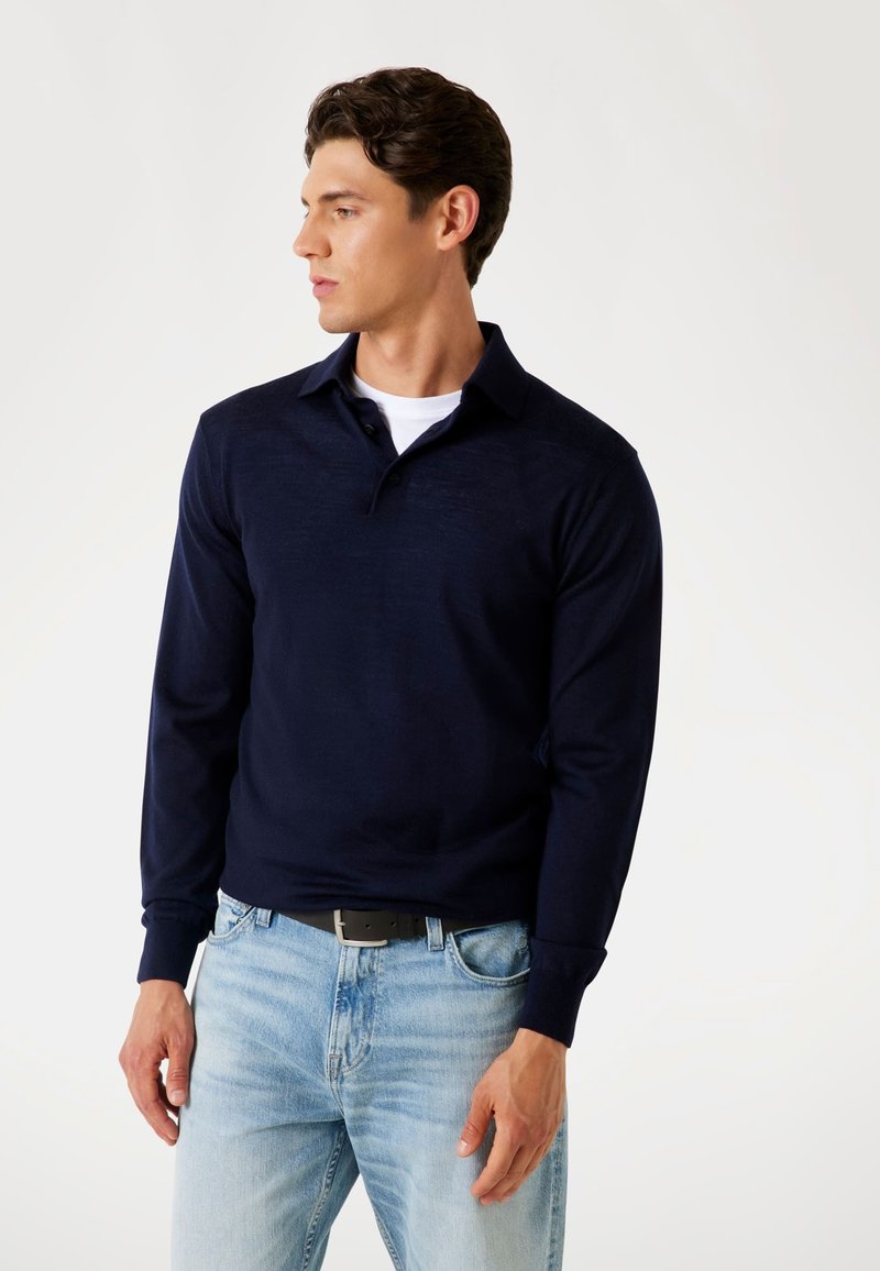 Dunkelblaues Langarm-Polohemd mit Kragen, aus strukturiertem Stoff, kombiniert mit hellblauen Jeans und einem schwarzen Gürtel.