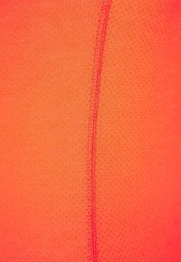 Tela de ropa deportiva de color naranja brillante con una textura lisa, que presenta una costura vertical y un diseño perforado para mayor transpirabilidad.