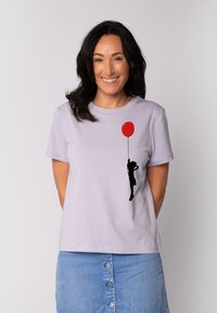 Helllila Baumwoll-T-Shirt mit einer schwarzen Silhouette einer Person, die einen roten Ballon hält, kurzen Ärmeln und einem lockeren Schnitt.