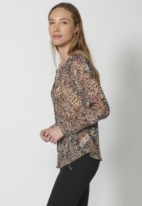 Blusa a maniche lunghe stampata in marrone e nero con scollo a V, caratterizzata da una consistenza leggera e trasparente e un orlo curvo.