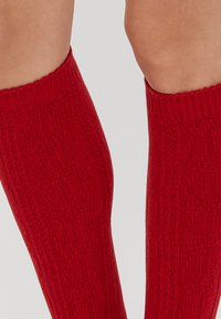 Czerwone skarpety do kolan z fakturowanym wzorem w zygzaki, żebrowanym górnym brzegiem oraz miękkim splotem materiału.