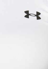 Camicia bianca aderente con un grande logo nero Under Armour sul petto. Il materiale appare liscio con una leggera lucentezza.