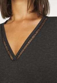 Zwarte V-hals shirt met een gestructureerd uitsnede detail langs de halslijn. De stof lijkt zacht, lichtgewicht en casual te zijn.