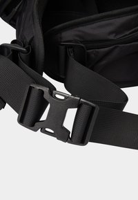 Black nylon backpack strap with a plastic buckle. Features adjustable webbing and textured surface for grip. Multiple attachment points visible.