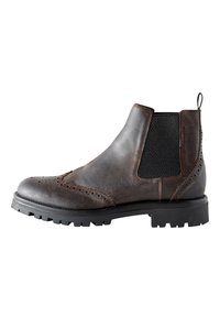 Brauner Chelsea-Stiefel aus Leder mit Brogue-Details, elastischen Seiteneinsätzen, strukturierter Oberfläche und einer robusten schwarzen Gummisohle.