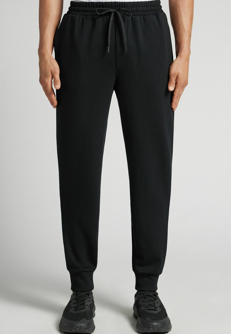 Czarne dresy z miękkiego materiału, z elastycznym pasem ze sznurkiem, lekko zwężanym krojem nogawek i bocznymi kieszeniami.