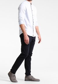 Chemise bleu clair à boutons avec col, associée à un pantalon slim noir et des bottines en daim gris. Design épuré et look décontracté.