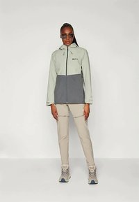 Šviesiai žalia ir tamsiai pilka neperšlampama striukė su užtrauktuku priekyje, reguliuojama kapuota ir dviem šoninėmis kišenėmis. Papildyta smėlio spalvos kelnėmis ir pilkomis avalynėmis.