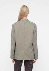 Szary w kratę żakiet o luźnym kroju, z klapami, długimi rękawami i centralnym szwem z tyłu. Teksturowana tkanina o dopasowanym fasonie.