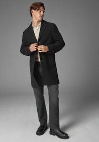 Palton negru din lână cu un design clasic, având reveruri tăiate, două butoane și buzunare frontale, combinat cu blugi gri și cizme negre.