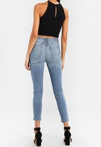 Top corto negro con cuello halter y detalle de abertura en la espalda, combinado con jeans ajustados de mezclilla azul claro y sandalias de tacón negro.