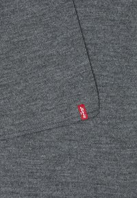 Tissu gris avec une texture lisse, doté d'une étiquette rouge Levi's cousue sur le bord, mettant en avant un design simple et minimaliste.