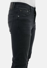 Zwarte denim jeans met een slim fit, voorzien van vijf zakken, een kleine metalen studs aan de voorkant en een leren label met textuur op de achterband.