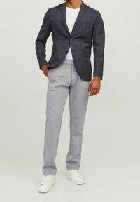 Blazer a quadri navy, pantaloni della tuta grigi e sneakers bianche. Il blazer ha due bottoni e un design aderente; i pantaloni della tuta sono elastici in vita.