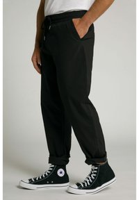 Pantalones jogger negros con una cintura elástica, detalle de cordón, bolsillos laterales y puños ajustados, combinados con zapatillas negras de caña alta.