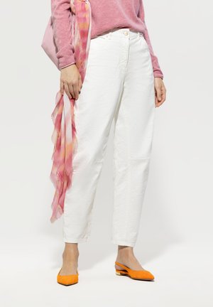 White, high-waisted jeans with side pockets and subtle seams; paired with a pink sweater and a sheer, patterned pink scarf, complemented by orange flats.