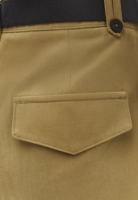 Pantalones de tela caqui con cierre de bolsillo solapa y cinturón negro visible en la cintura, mostrando costuras y textura detalladas.