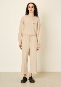 Beige sweatshirt med ribbet tekstur, der har et lille multicolor logo, parret med matchende cropped bukser og sorte slip-on sko.