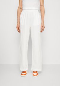 Pantalons larges blancs avec une taille élastique, en tissu léger, poches avant, associés à des baskets orange et crème.