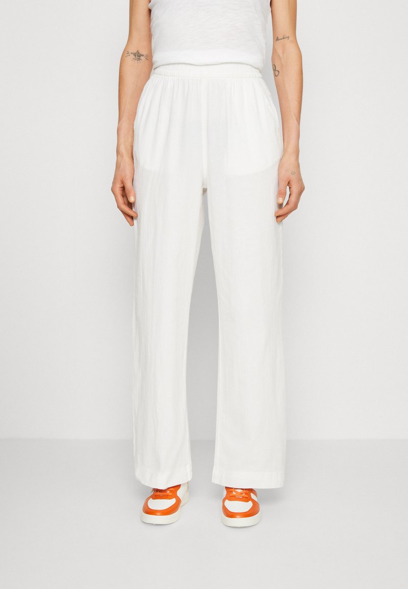 Pantalons larges blancs avec une taille élastique, en tissu léger, poches avant, associés à des baskets orange et crème.