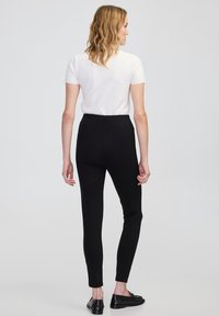 Czarne dopasowane spodnie z wysokim stanem i długością do kostek, w połączeniu z białą bluzką z krótkim rękawem. Gładka tekstura, minimalistyczny design.
