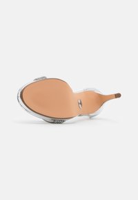 Sandale à talon transparent avec une semelle en caoutchouc brun, des accents argentés et un design supérieur transparent. Le talon est courbé avec une silhouette élancée.