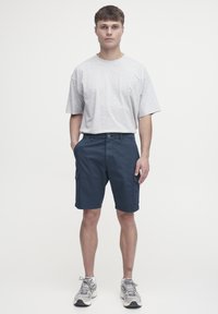 Graues kurzärmeliges T-Shirt kombiniert mit marineblauen Cargo-Shorts mit Taschen und geradem Schnitt. Sneakers vervollständigen das Outfit.