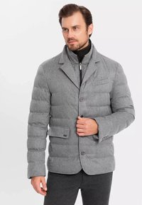 Chaqueta gris acolchada con diseño de blazers, que presenta un cuello con muesca, botones frontales y un bolsillo en el pecho, fabricada en tejido texturizado.