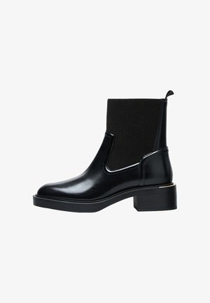 Schwarze Ankle Boots mit einem glänzenden Lederoberteil, gerippten elastischen Seitenpaneelen und einem Blockabsatz, der mit einem goldenen Akzent verziert ist.