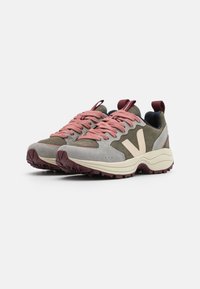 Tenis de camurça cinza e verde oliva com atacadores cor-de-rosa e logotipo bege contrastante. Sola de borracha grossa com um padrão texturizado para aderência.